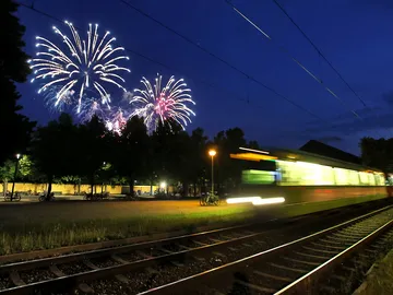Eine ÜSTRA Stadtbahn fährt vorbei und im Hintergrund ist das Feuerwerk am Abendhimmel zu sehen.