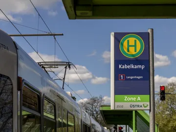 Im Fokus des Bildes ist das Haltestellenschild der Haltestelle "Kabelkamp" zu sehen. Im Hintergrund blauer Himmel mit weißen Wolken, am linken Bildrand lässt sich eine Stadtbahn erkennen. 