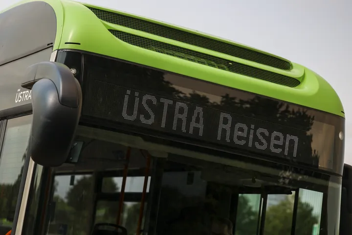 Zu sehen ist die digitale Anzeige eines grünen Busses. Darin steht ÜSTRA Reisen.