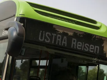 Zu sehen ist die digitale Anzeige eines grünen Busses. Darin steht ÜSTRA Reisen. 