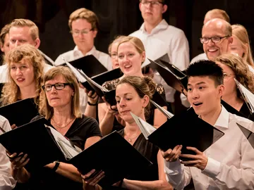 Mehrere Chormitglieder halten ein Gesangsbuch in der Hand und singen.