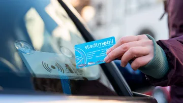 Nahaufnahme auf eine Hand, die eine stadtmobil-Karte im Scheckkartenformat an die Windschutzscheibe eines stadtmobil-Autos hält, um es zu entriegeln.