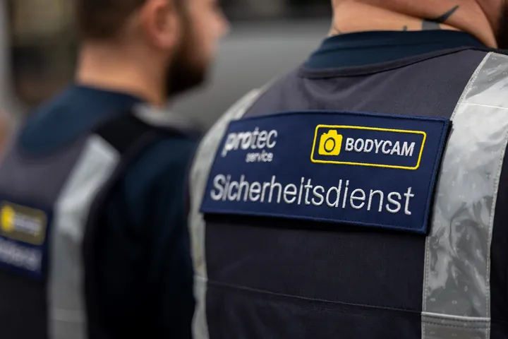 Der Rücken zweier protec-Mitarbeiter, die mit einem Aufnäher mit der Aufschrift Aicherheitsdienst und Bodycam versehen sind.