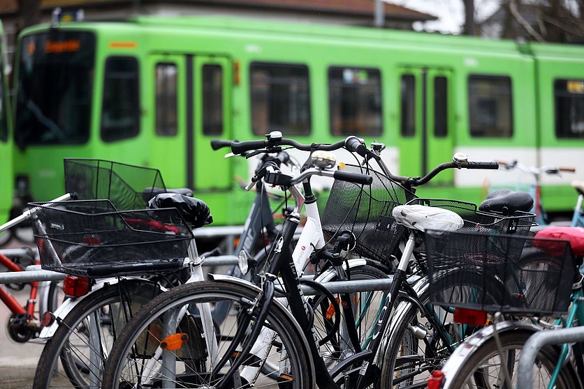 Bild von mehreren Fahrrädern an einem Stellplatz. Im Hintergrund fährt eine Stadtbahn