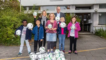 Die ÜSTRA Vorständin Elke Maria van Zadel und Ulf Birger Franz übergeben der Schulleitung und den Kindern der Grundschule die Bälle