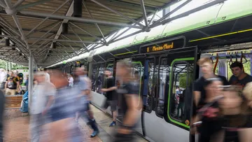 Personen steigen aus der Bahn an der Haltestelle Messe Nord, um zu einer Veranstaltung auf dem Messegelände zu gehen 