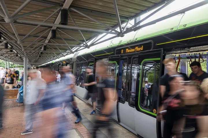 Personen steigen aus der Bahn an der Haltestelle Messe Nord, um zu einer Veranstaltung auf dem Messegelände zu gehen