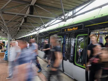 Personen steigen aus der Bahn an der Haltestelle Messe Nord, um zu einer Veranstaltung auf dem Messegelände zu gehen 