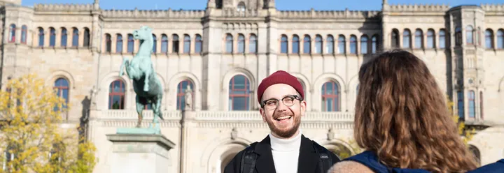 Zwei jüngere Menschen stehen vor der Ernst-August-Universität in Hannover und sprechen miteinander