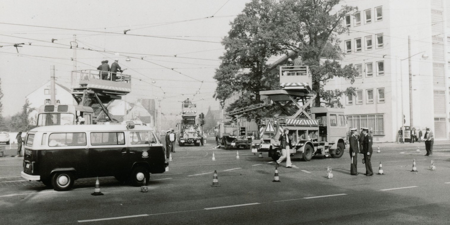 Vier Oberleitungsfahrzeuge mit Personal arbeiten an der Oberleitung. Im Vordergrund steht ein VW Bus der Polizei. Mehrere Polizisten stehen bereit, um den Verkehr zu regeln.