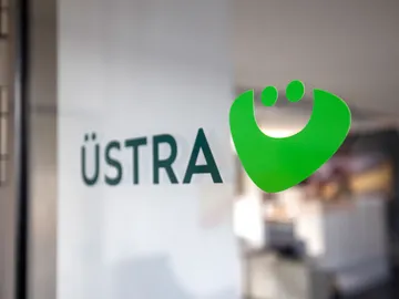 Das Logo der ÜSTRA auf einer Glastür. Im Hintergrund sieht man verschwommen ein Büro.
