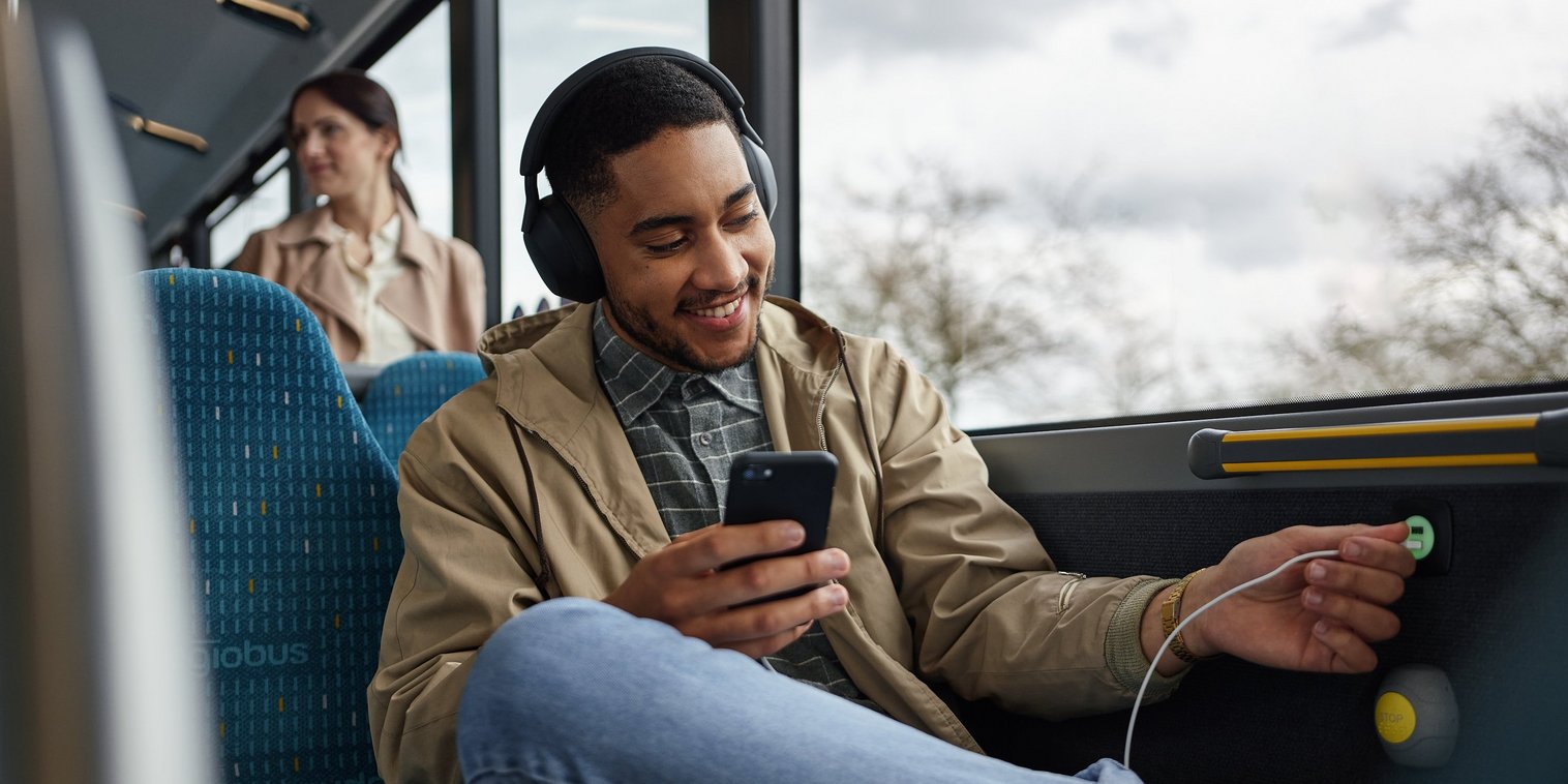 Junger Mann lädt sein Smartphone per USB im Bus.