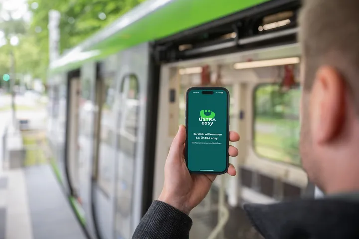 Fahrgast vor Stadtbahn in Hannover mit Handy in der Hand. Abgebildet ist ein Screen mit der neuen ÜSTRA easy App, mit der ein digitales Ticket gekauft werden kann. 
