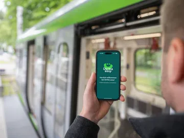 Fahrgast vor Stadtbahn in Hannover mit Handy in der Hand. Abgebildet ist ein Screen mit der neuen ÜSTRA easy App, mit der ein digitales Ticket gekauft werden kann. 