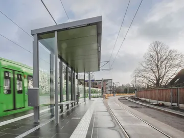 Der Hochbahnsteig mit Wartehäuschen der Haltestelle Riechersstraße im Regen. Ein TW 6000 fährt ein. 