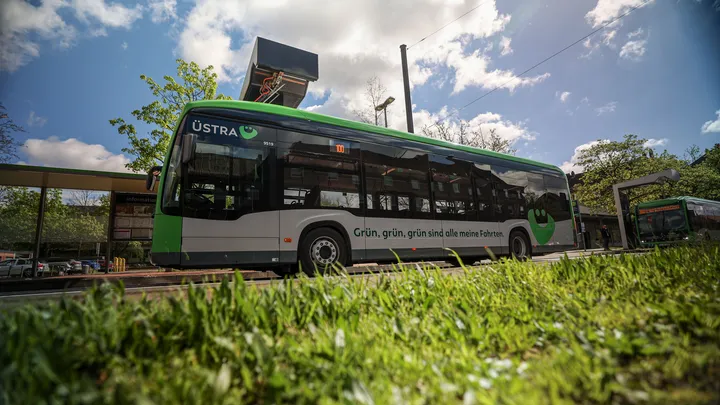 Ein Elektrobus der Marke Mercedes steht am August-Holweg-Platz in Hannover. Der Bus lädt gerade die Batterien über die Ladesäule auf. Auf dem Bus ist eine Werbung mit dem  Slogan "Grün, grün, grün, sind alle meine Fahrten!" angebracht.
