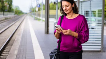 Berufspendlerin steht mit Handy an Haltestelle