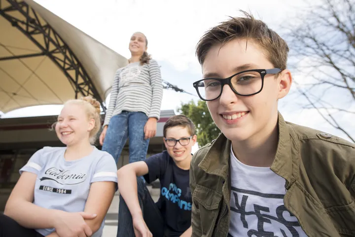 Mehrere Kinder stehen vor einem Veranstaltungsort. Ein Junge lacht in die Kamera. 