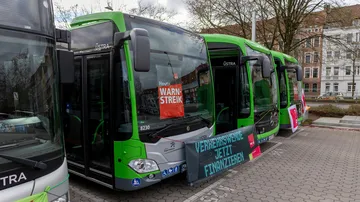 Vier Busse stehen nebeneinander auf dem Betriebshog und sind mit ver.di Streikpostern und Bannern "geschmückt".