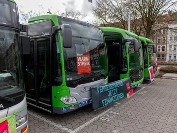 Vier Busse stehen nebeneinander auf dem Betriebshog und sind mit ver.di Streikpostern und Bannern "geschmückt".