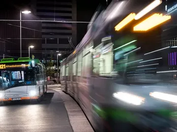 Bus steht bei Nacht an einer Haltestelle während Stadtbahn vorbeifährt.