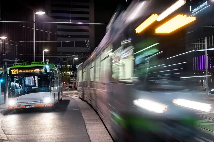 Bus steht bei Nacht an einer Haltestelle während Stadtbahn vorbeifährt.