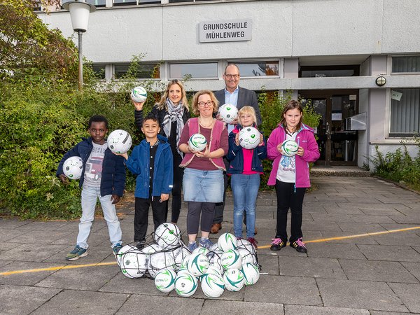 Elke van Zadel und Ulf Birger Franz überreichen Kindern und der Schulleitung Bälle. 