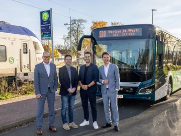 Bei dem Pressetermin in Weetzen verkünden Regionspräsident Steffen Krach, Verkehrsdezernent Ulf-Birger Franz und Vertreter der Gemeinde die Verlängerung zum Bahnhof Weetzen. Sie stehen vor dem Bus, im Hintergrund kann man eine S-Bahn sehen.