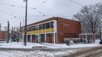 Das Bild zeigt das Hofdienstgebäude der ÜSTRA auf dem Betriebshof Glocksee von der Seite. Es liegt Schnee. Das Haus ist aus rotem Klinker gebaut und hat eine teilweise gelbe Fassade.