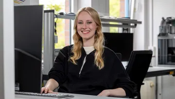 Eine junge Frau sitzt an einem Büroarbeitsplatz. 