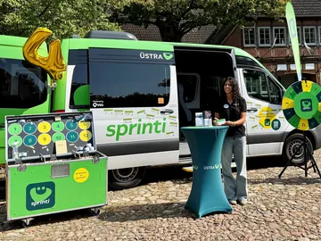 Ein sprinti Fahrzeug steht auf der Roadshow mit offenen Türen und davor ein Glücksrad und verschiedenes Veranstaltungsequipment.