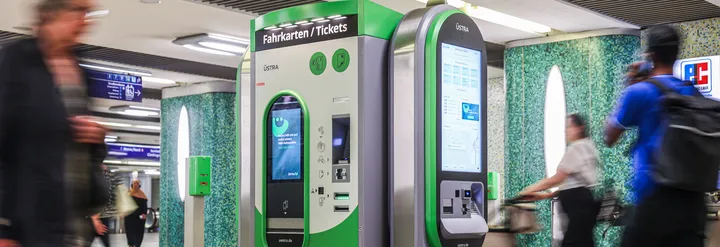 Ein Fahrtkartenautomat der ÜSTRA in der Station Kröpcke. Rechts, links und im Hintergrund des Bildes sind Menschen zu sehen, die leicht verschwommen sind.