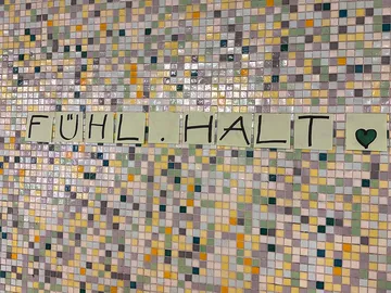 Auf einer Mosaik-Wand kleben Klebezettel mit den Worten Fühl.Halt.
