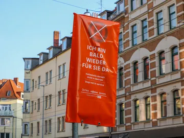 Ein Haltestellenmast mit orangem Überzug. Darauf steht: "Ich bin bald wieder für Sie da"