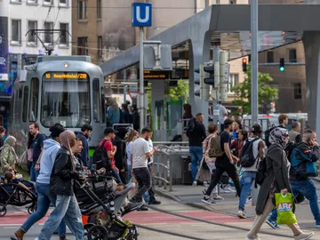 Menschen gehen über die Straße an der oberirdischen Haltestelle Steintor. An dieser Hält gerade eine Stadtbahn.