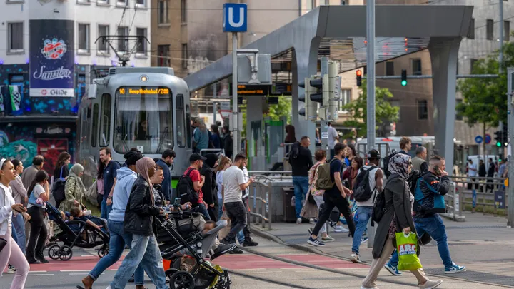 Menschen gehen über die Straße an der oberirdischen Haltestelle Steintor. An dieser Hält gerade eine Stadtbahn.
