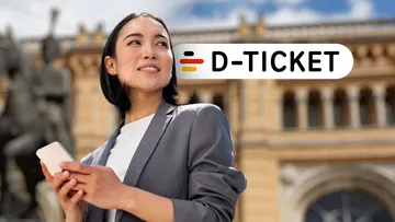 Frau steht vor Hauptbahnhof in Hannover, Handy in der Hand und schaut sich um, außerdem ist ein Logo des Deutschlandtickets im Bildmotiv