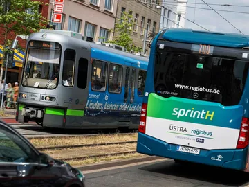 Eine ÜSTRA-Straßenbahn und ein Bus von regiobus fahren aneinander vorbei.