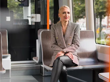 Regine Oelfke sitzt mit überschlagenen Beinen in einer Stadtbahn und blickt in die Kamera