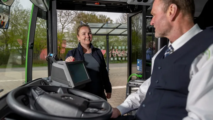 Fahrer im Bus sitzend spricht mit einsteigendem weiblichem Fahrgast 