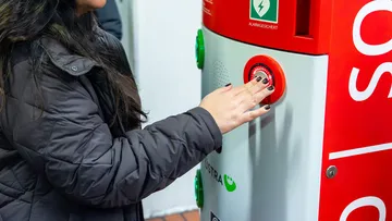 Eine Frau mit schwarzer Jacke drückt den Notfallknopf an der Notruf-und Informationssäule, die in den Tunnelstationen von Hannover steht.